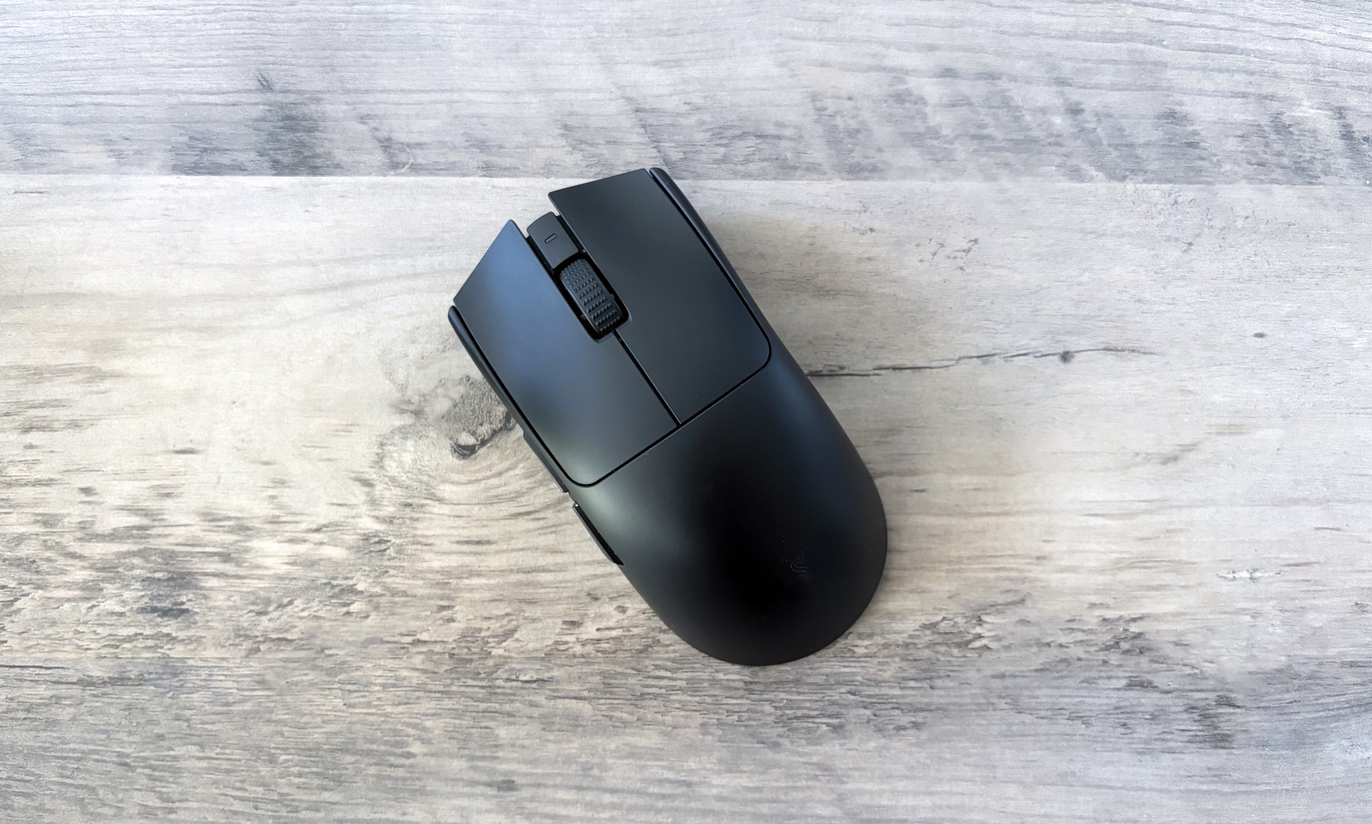 A black Razer Viper V3 Pro gaming mouse rests slightly angled on top of a light brown wooden table.