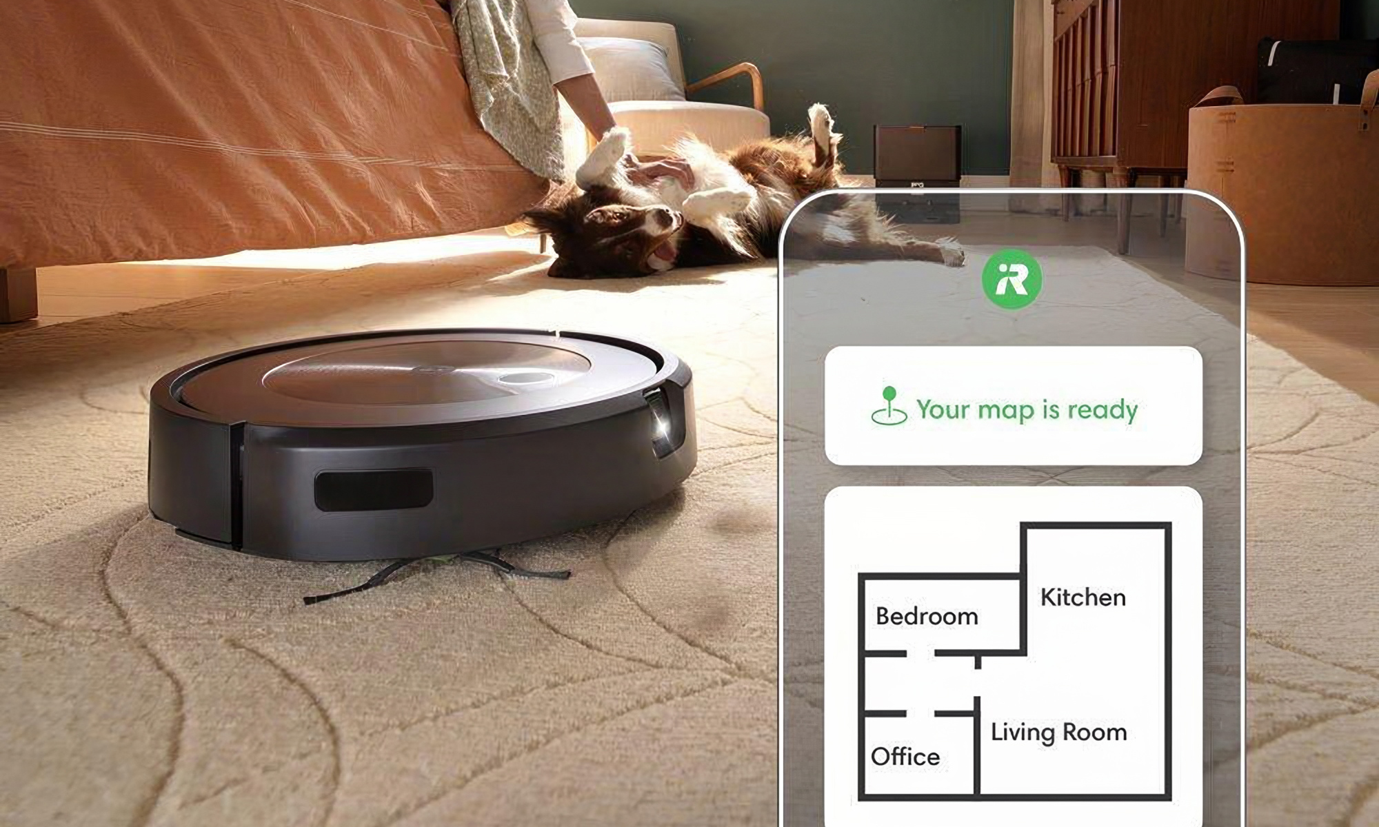 Product lifestyle photo for the iRobot Roomba j9+. The device vacuums an area rug while a dog gets a belly rub in the background. Overlaid is a home map from the Roomba app.