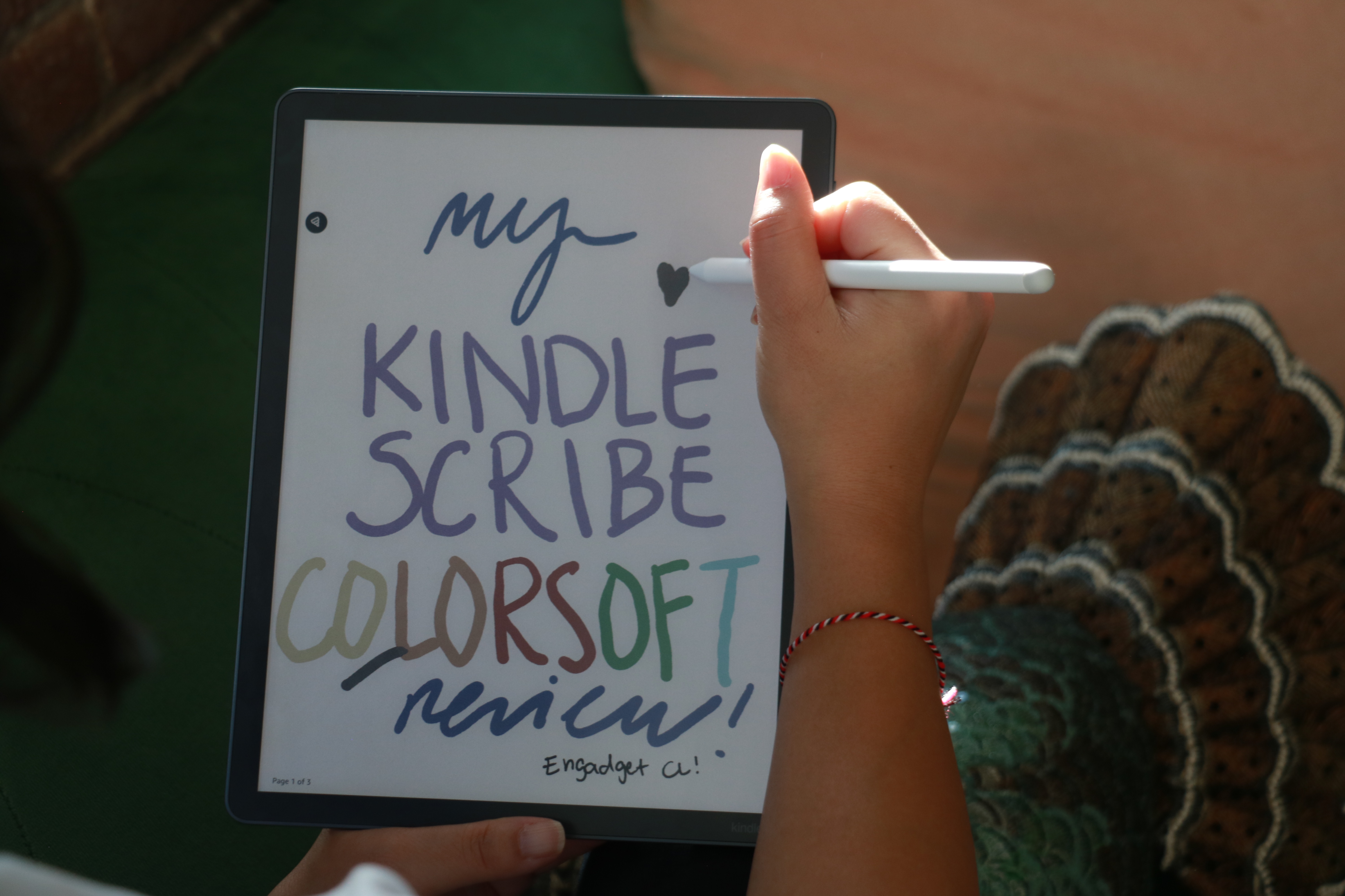 A person holding the Kindle Scribe Colorsoft in their left hand while holding the Premium Pen in their right, finishing off a drawing of a heart on the device.