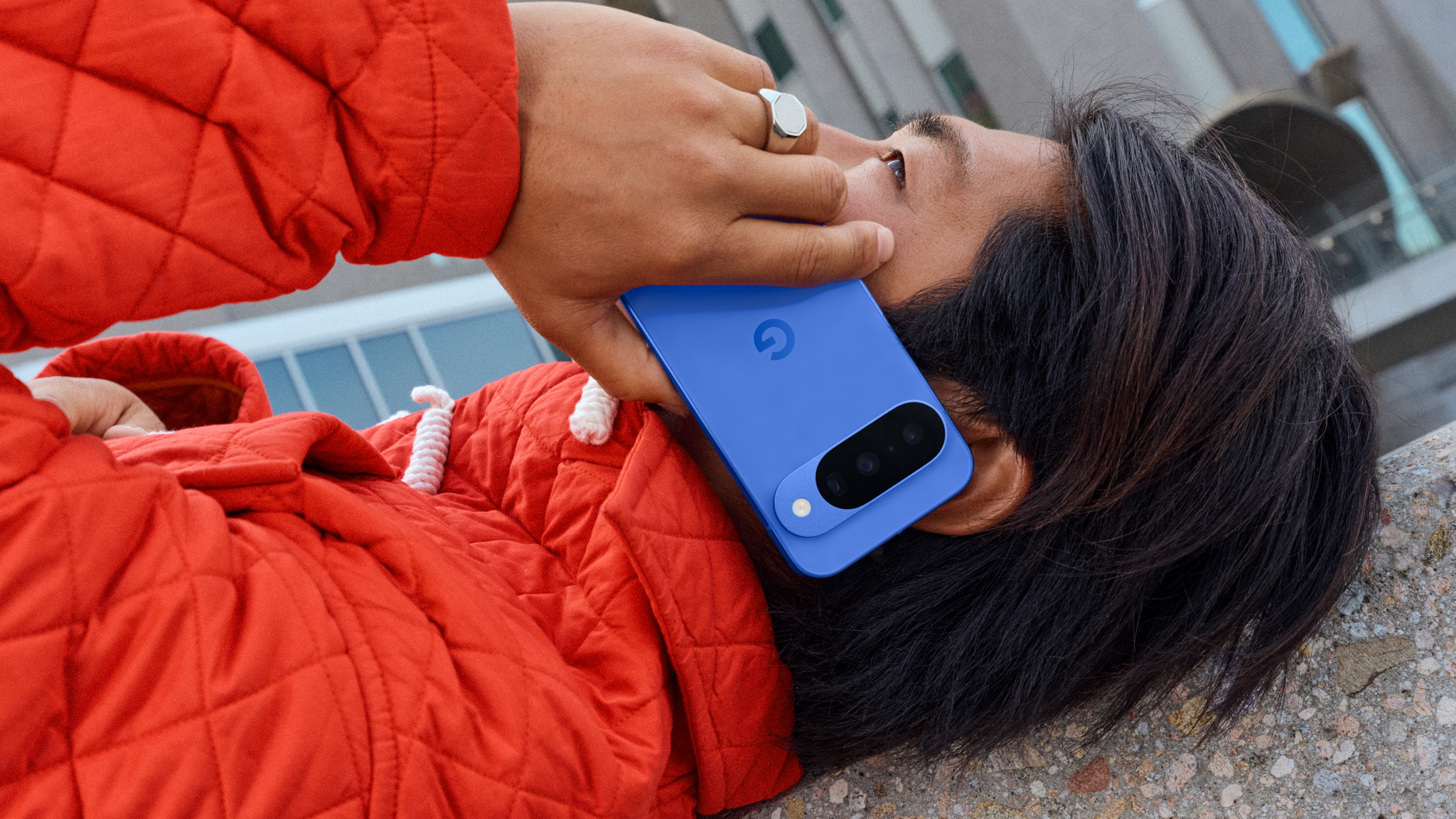 A person lying on a granite surface, talking on a blue Pixel 10 phone.