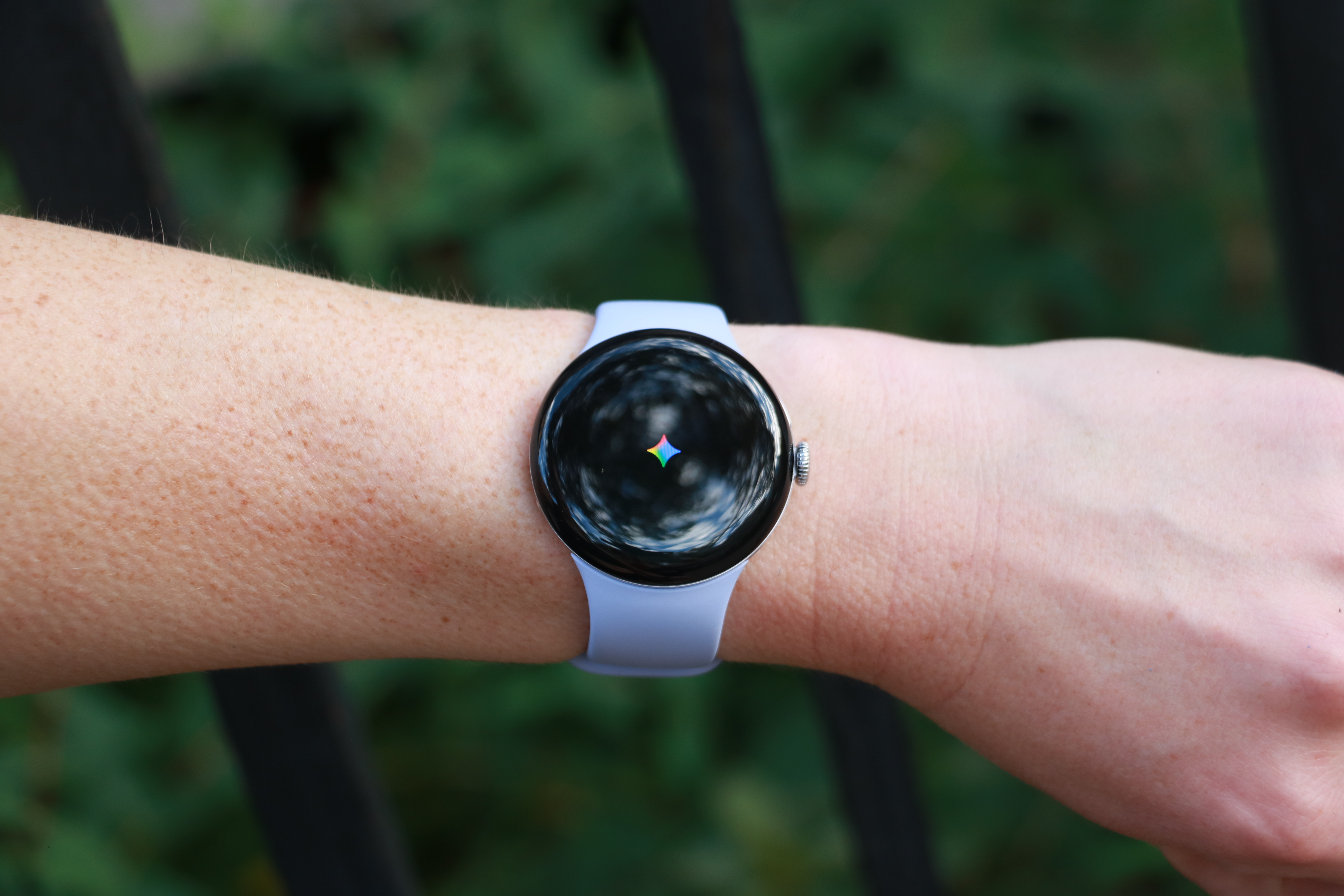 The Pixel Watch 4 on a wrist held up in mid-air, with the Gemini logo on its screen.