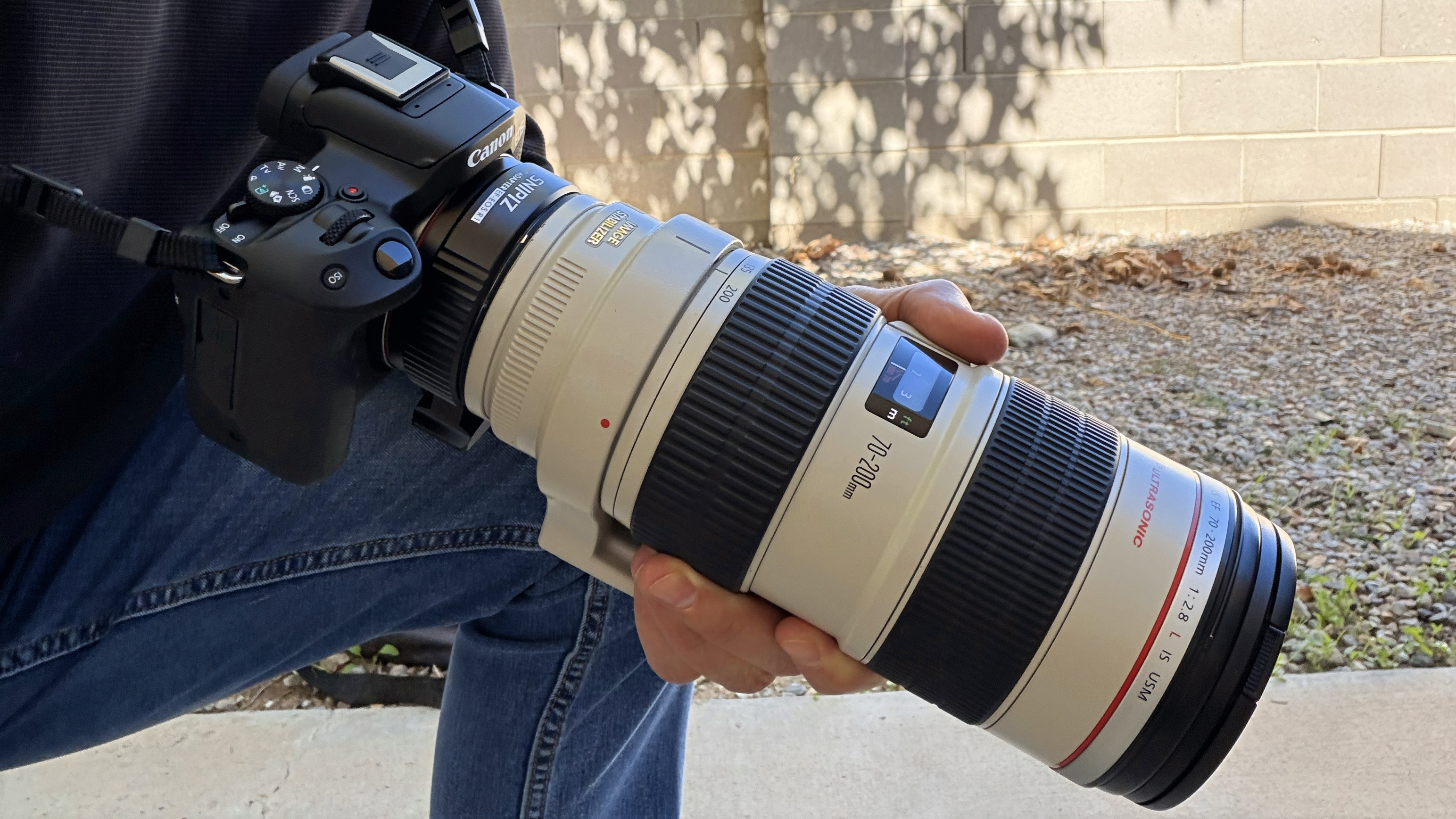 A person holding the compact Canon EOS R50 with a very long 70-200 lens attached.