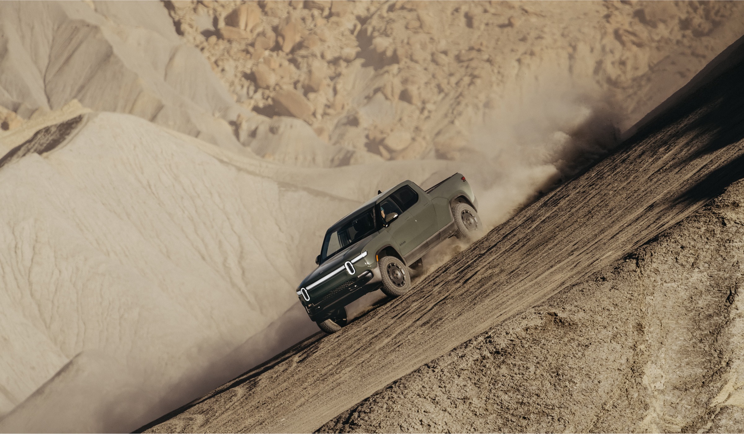 A Rivian R1T Quad EV truck driving on a steep dirt hillside.