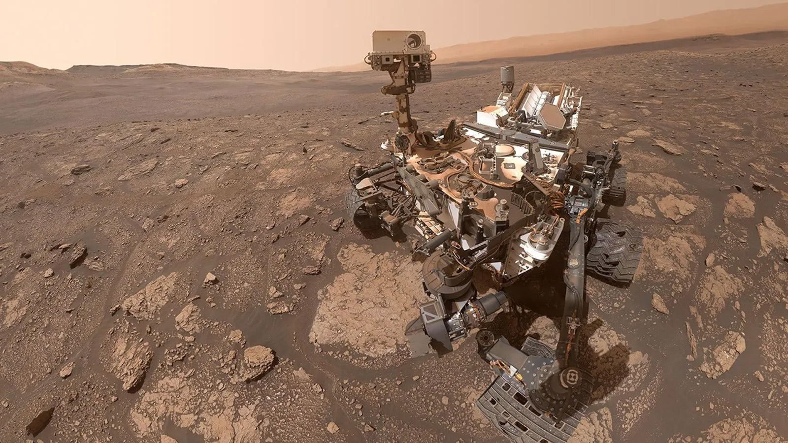 A selfie taken by the Curiosity rover on Mars. The rover sits on the reddish-brown, rocky surface.