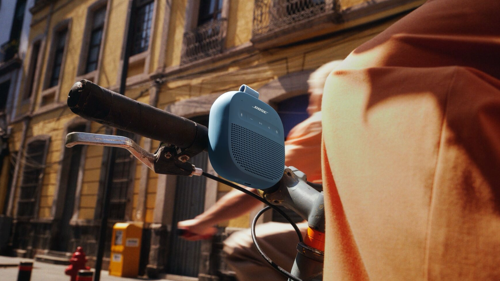 Closeup of a bicycle handlebar, with the Bose speaker strapped to it.