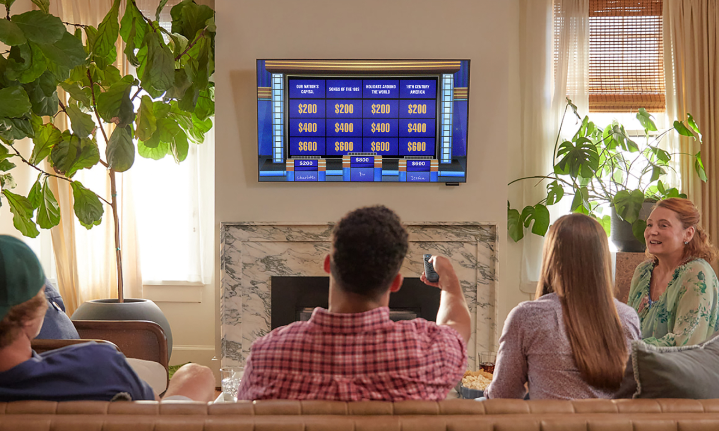Product lifestyle image of a group of friends in a living room playing Jeopardy! on their TV.