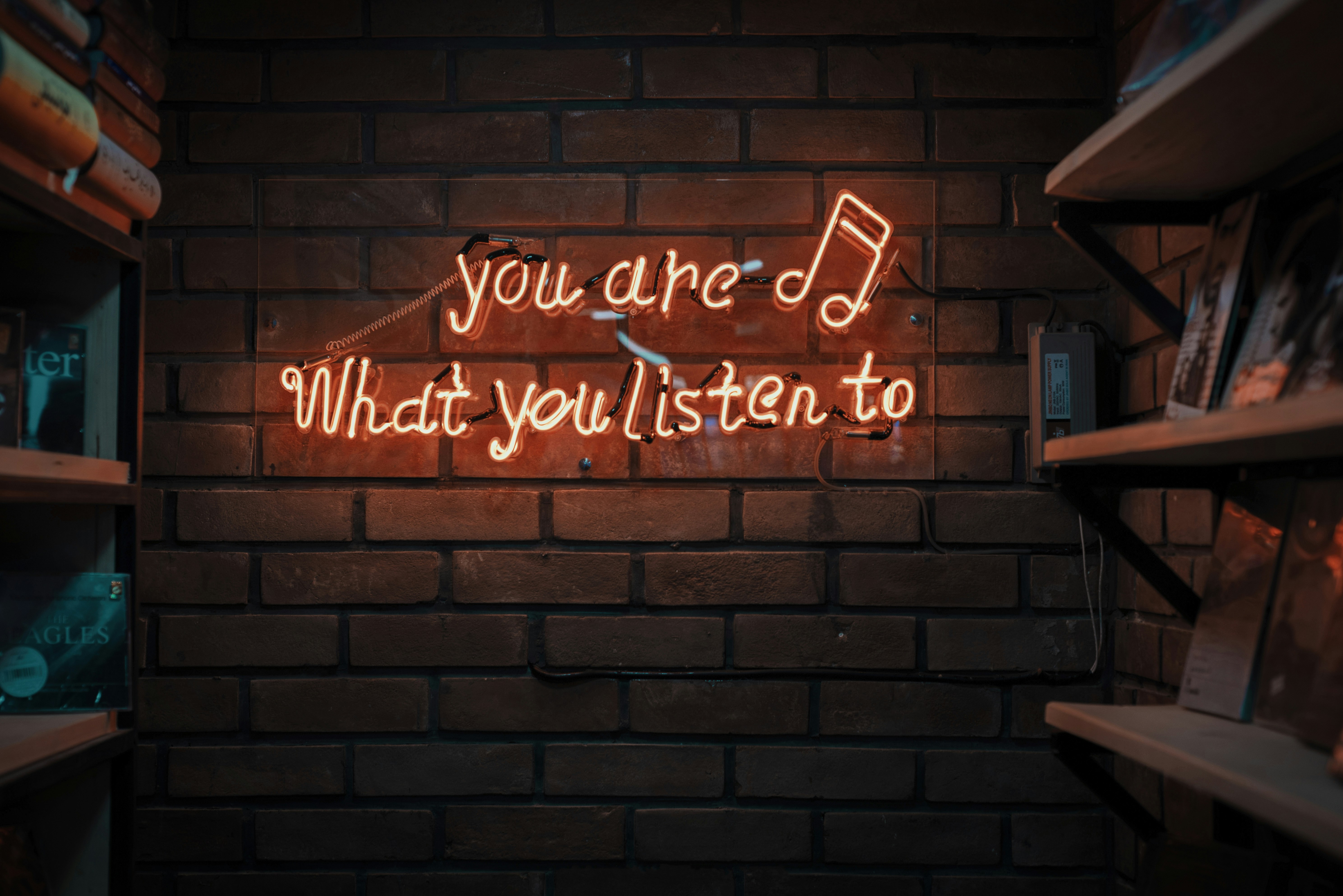 A neon sign on a wall, reading, You are what you listen to.