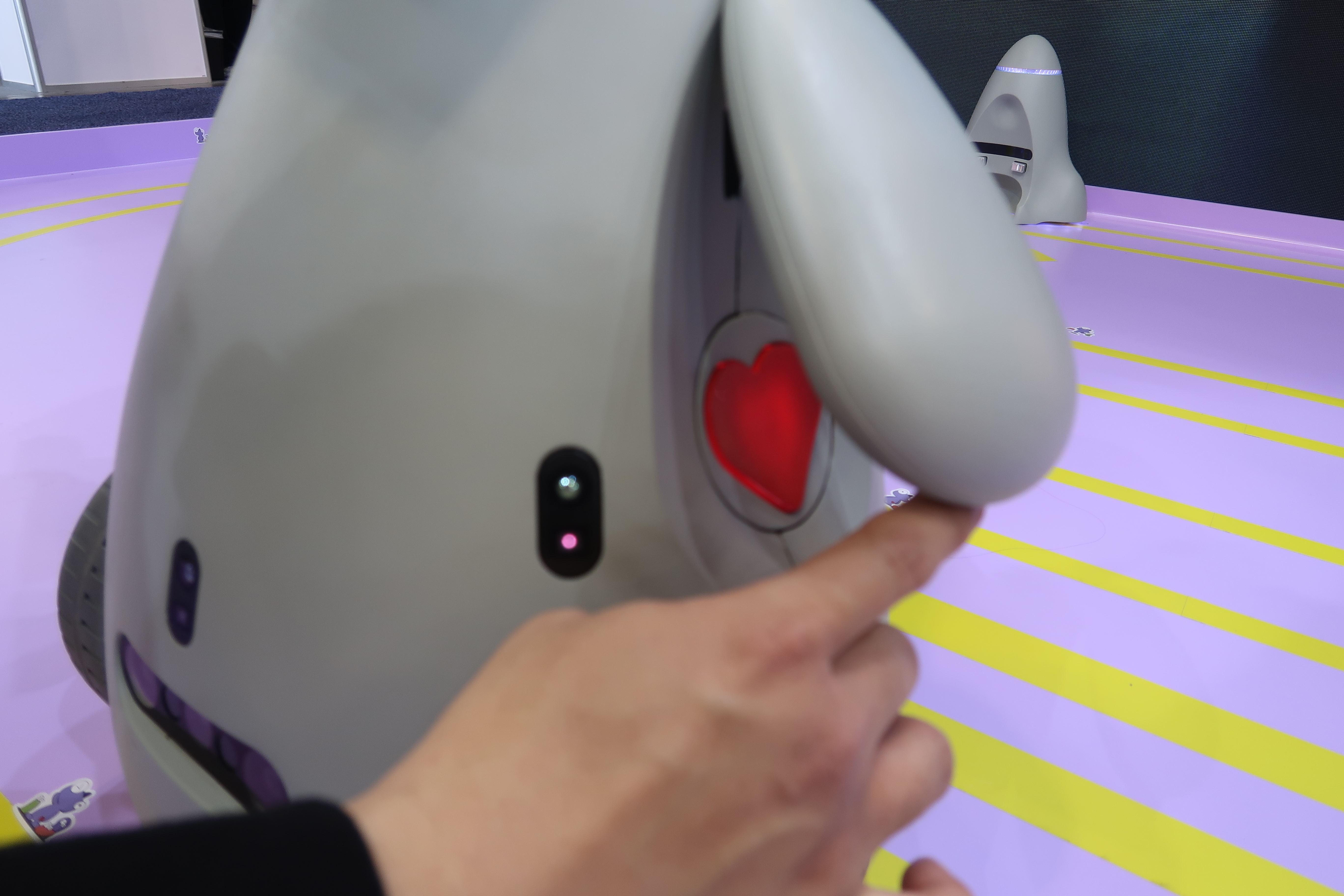 A hand is seen lifting OlloBot's arm to reveal a red heart underneath, which serves as a removable module that contains its data