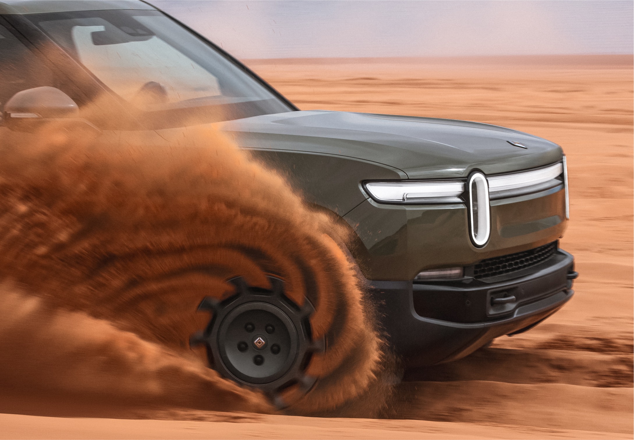 A Rivian R1 Quad EV kicking up dirt in an open desert.