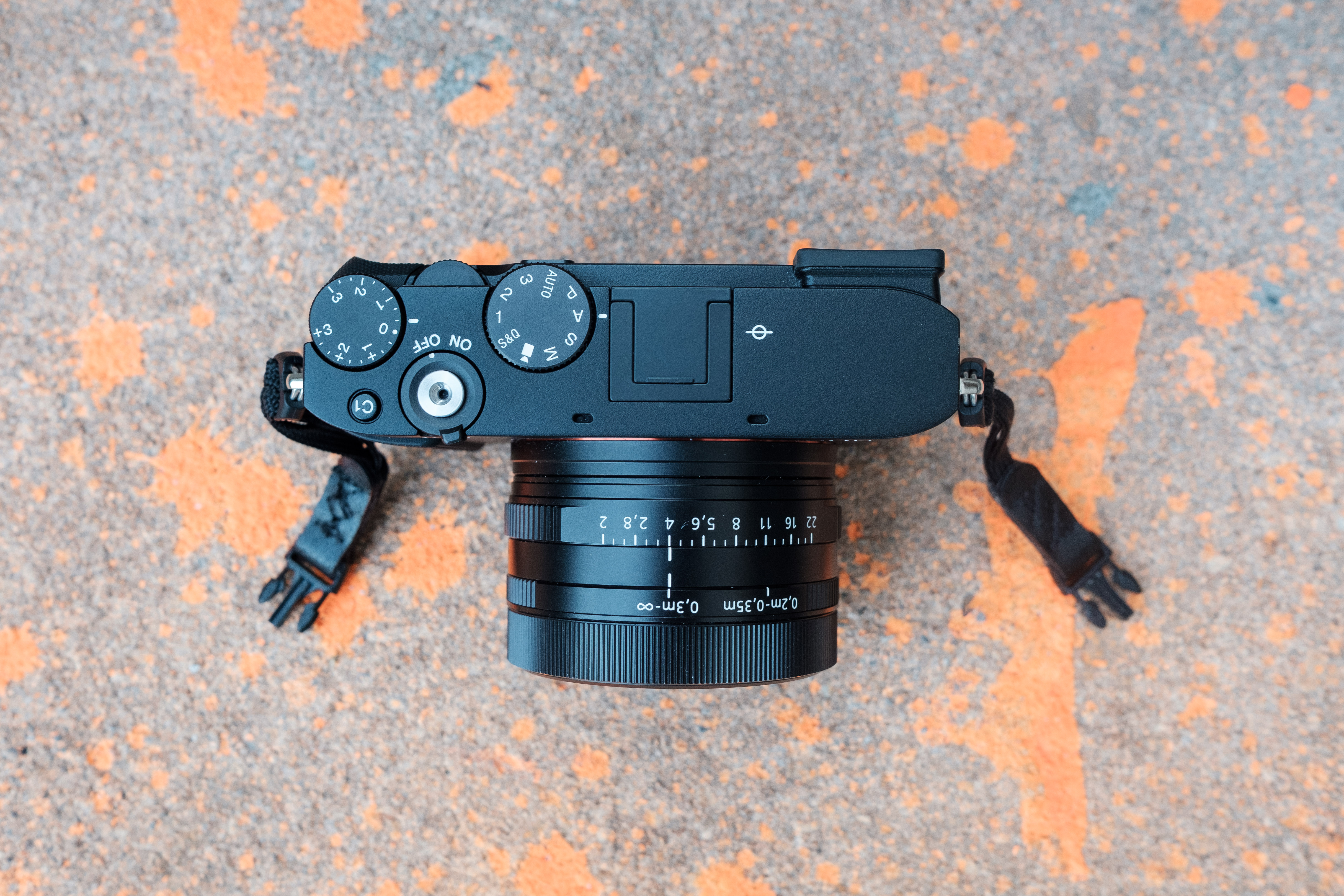 A overhead shot of the RX1R III showing the camera's top dials. It sits on concrete that has splatters of orange paint. 