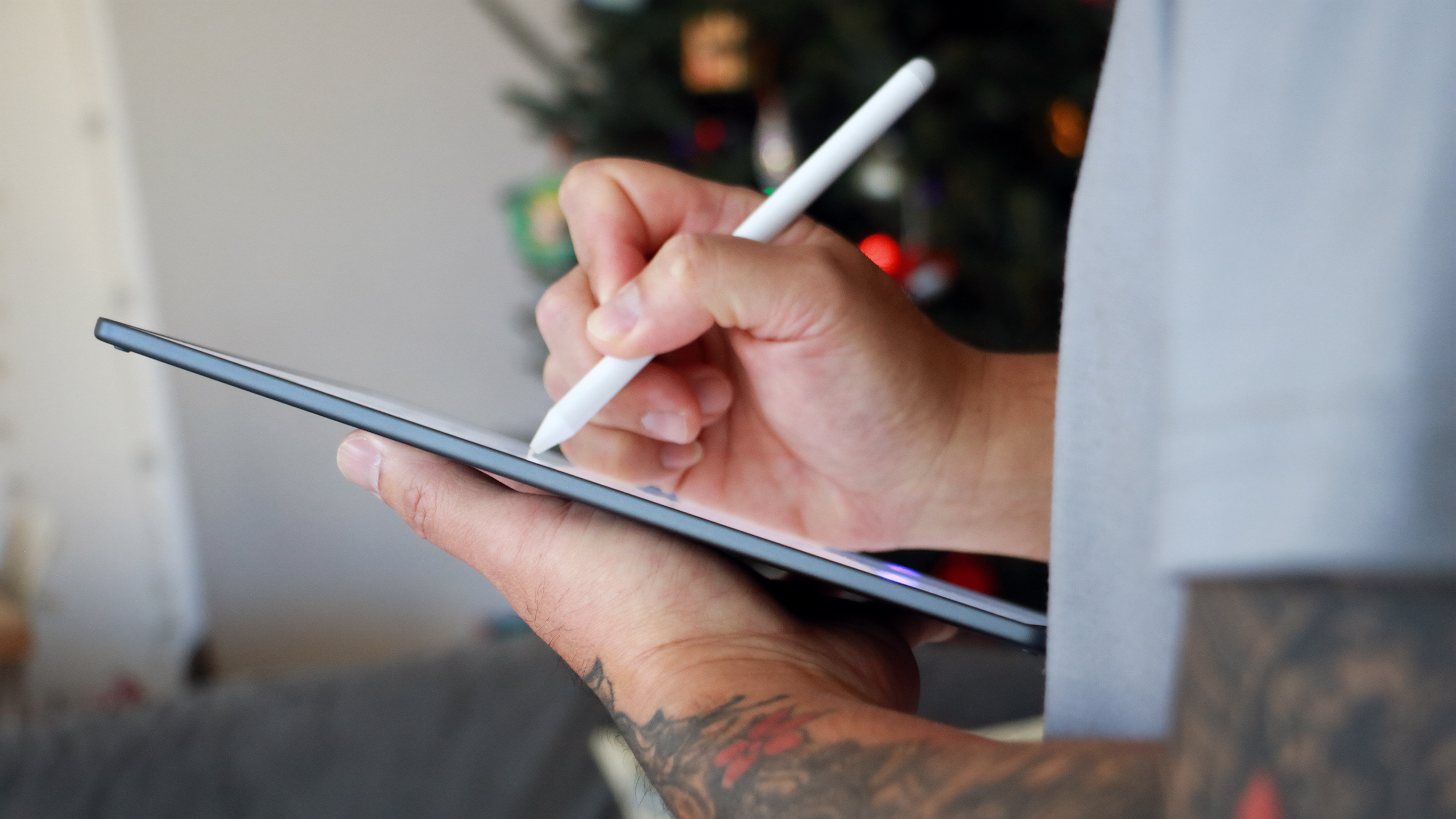 Side view of a person holding the Kindle Scribe Colorsoft in one hand and holding Amazon's Premium Pen in their other hand to write on the screen.