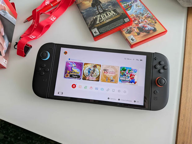 Image of a Nintendo Switch 2 on a white table, alongside a Lanyard, and a copy of Breath of the Wild and Mario Kart world.