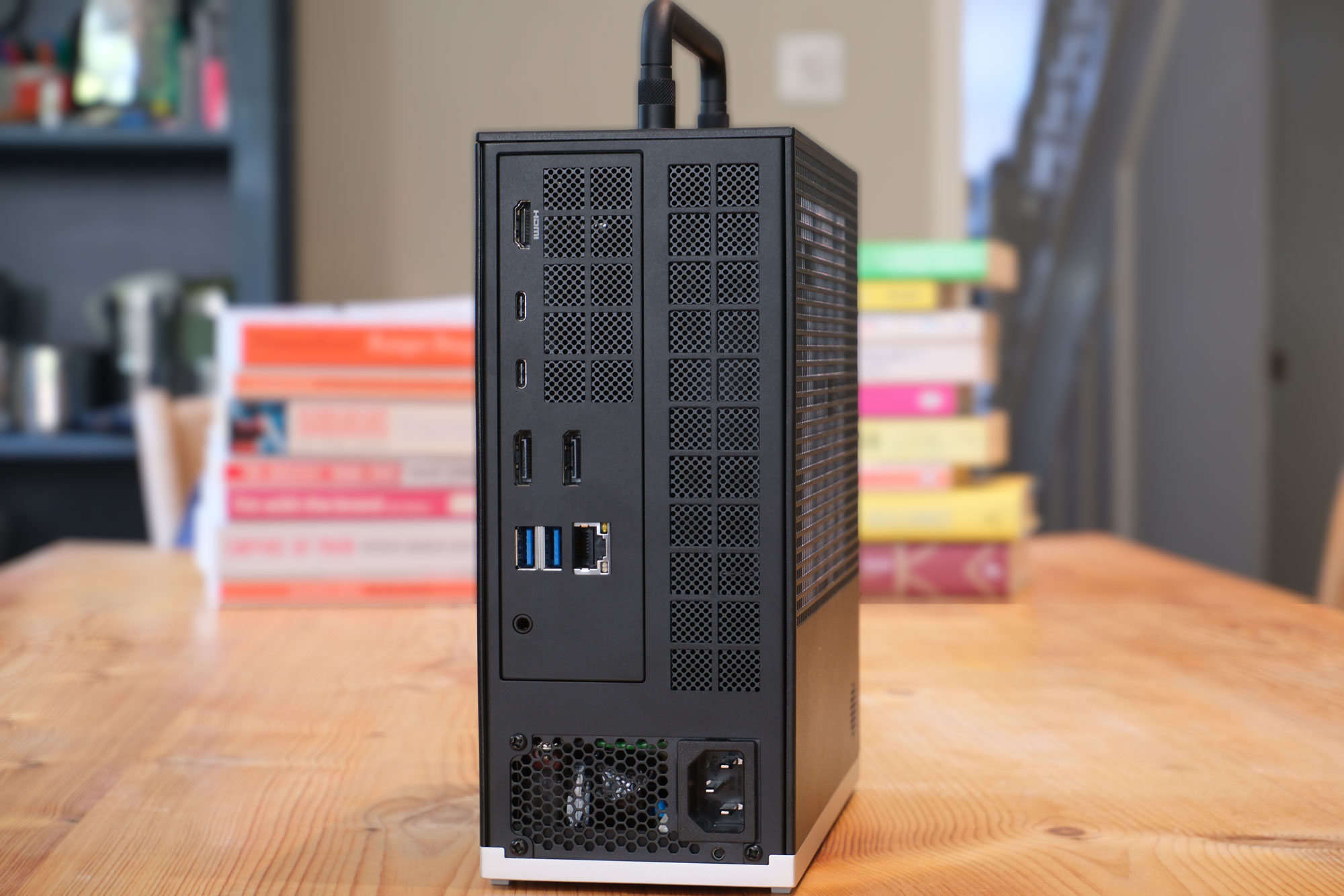 Image of the rear of the Framework Desktop (2025) sat on a wooden table in front of some books. The focus is on its port selection.