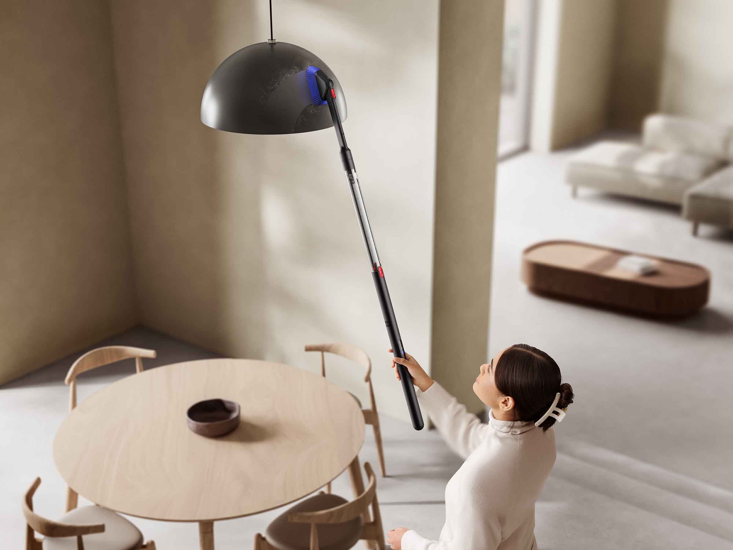 A person using the Dyson PencilVac to clean an overhead light fixture.