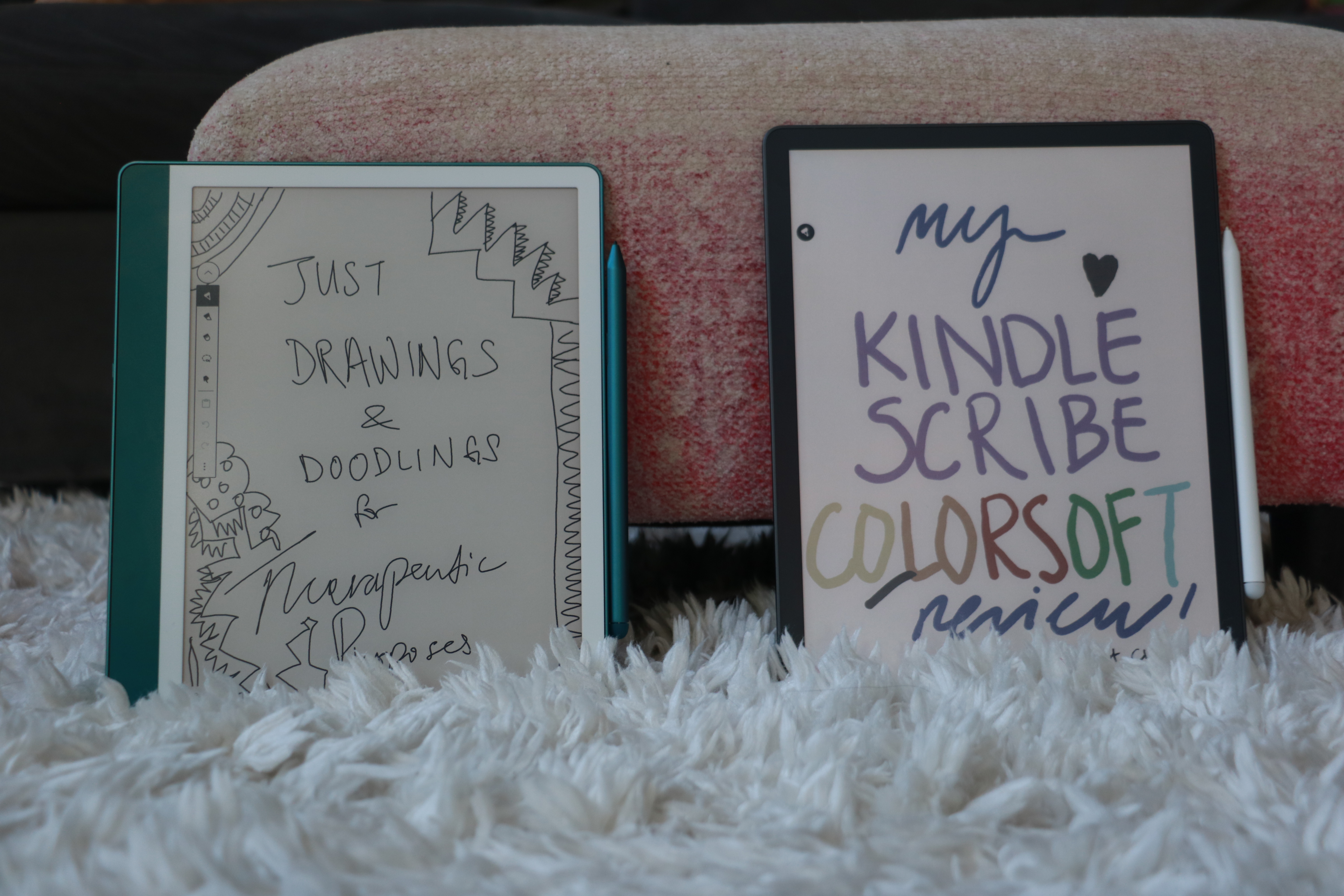 The 2024 model of the Kindle Scribe propped up next to the Kindle Scribe Colorsoft, each showing hand-drawn words and doodles on their screens.